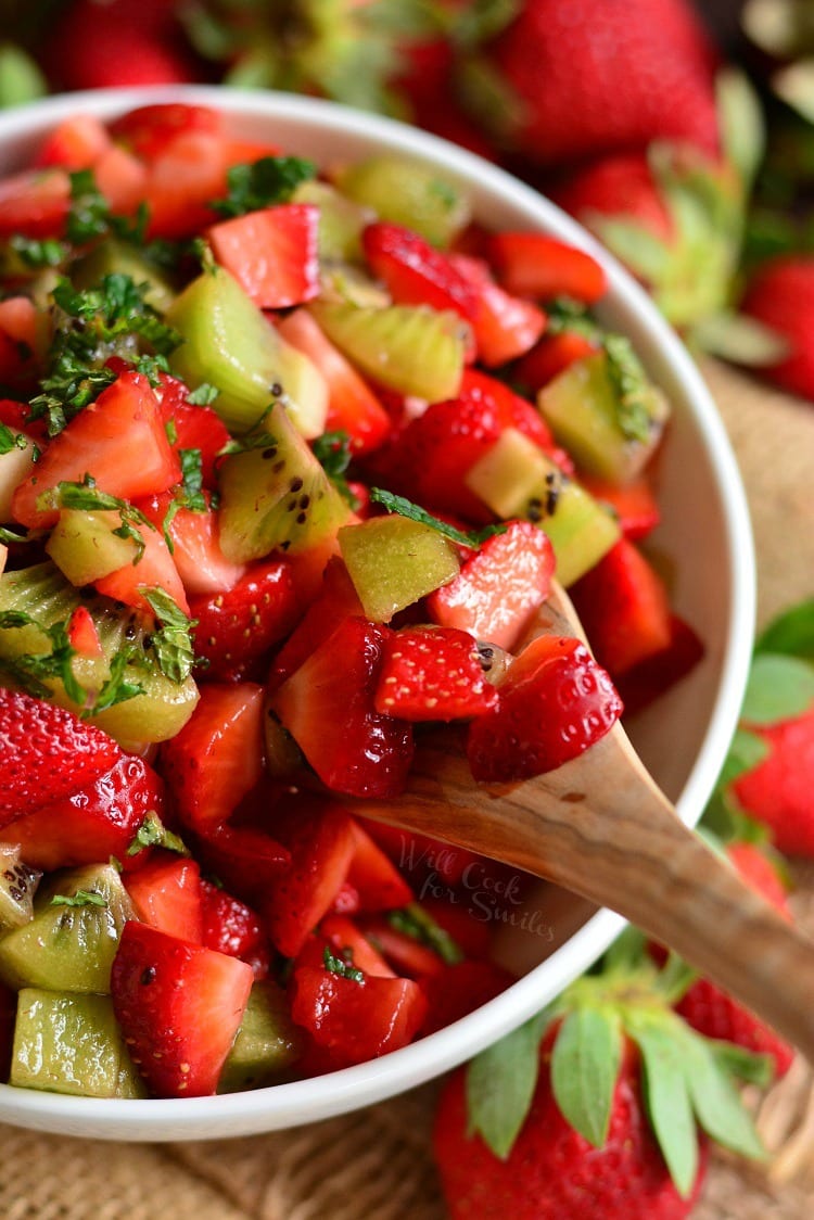 strawberry and kiwi fruit salad with a wooden spoon lifting some out.