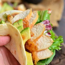 holding a soft taco with chicken, lettuce, and avocado.