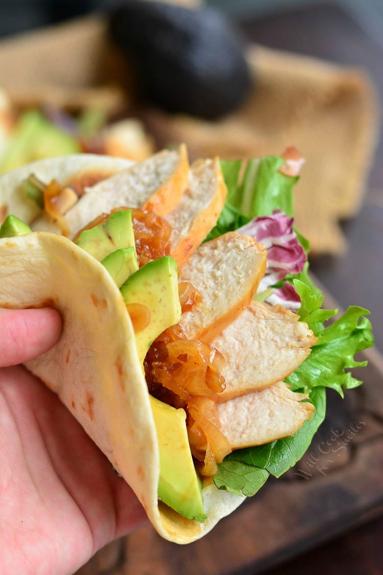 holding a soft taco with chicken, lettuce, and avocado.