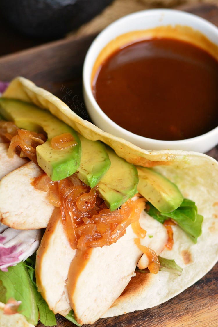 chicken in a soft taco with avocado and a side of sauce.