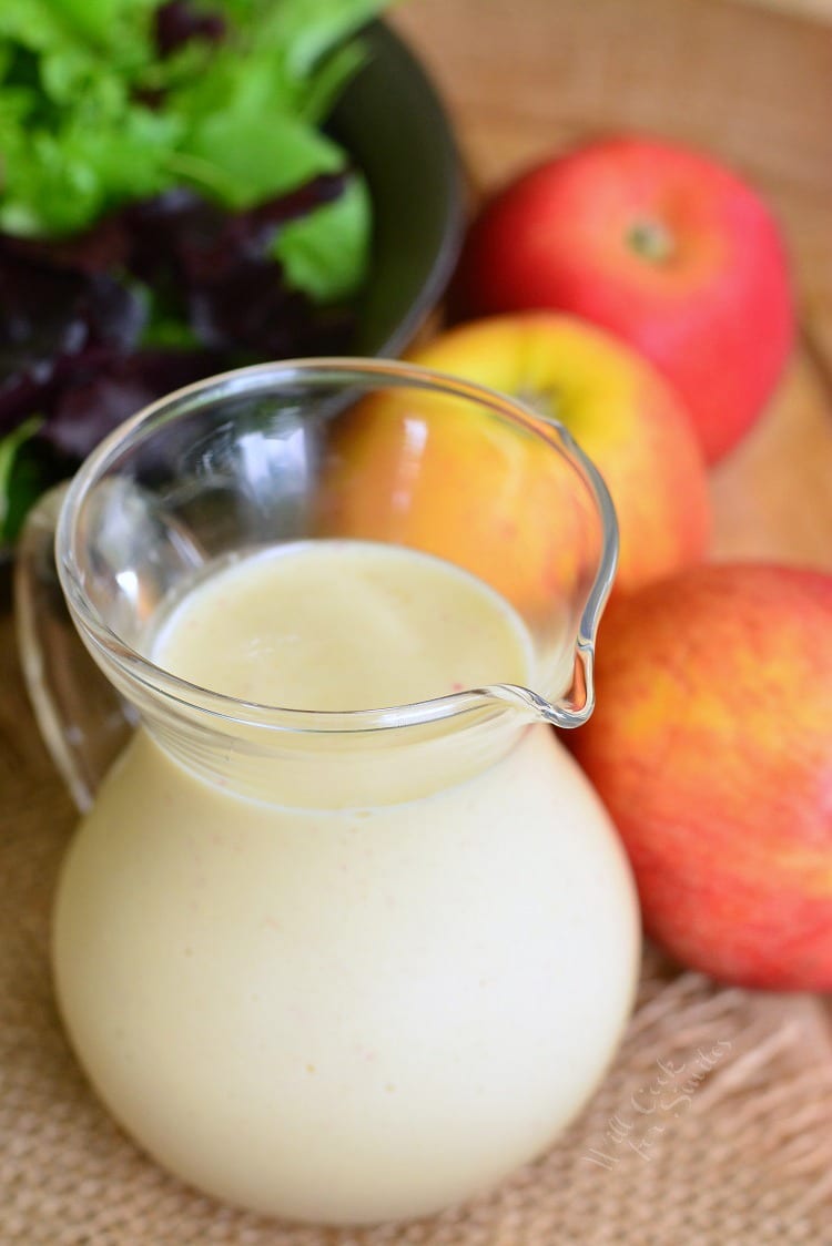 Delicious homemade Apple Vinaigrette in a glass container on a wood table with apples and salad in the background 