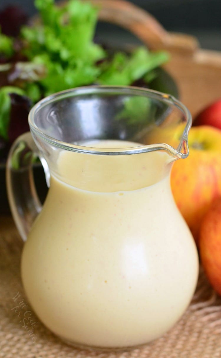 Delicious homemade Apple Vinaigrette in a glass container on a wood table with apples and salad in the background 