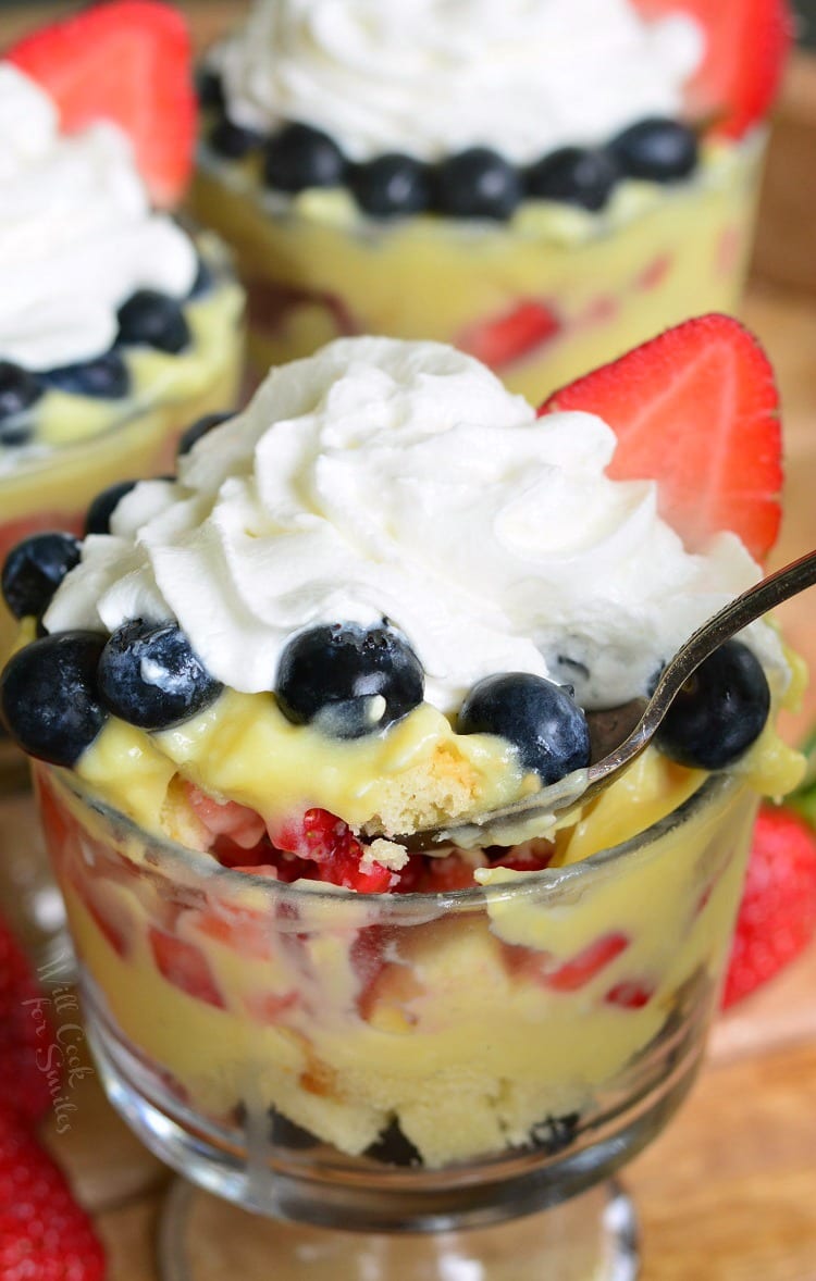 Easy Coconut Berry Trifle in a glass serving bowl with a spoon on a cutting board with a strawberries 