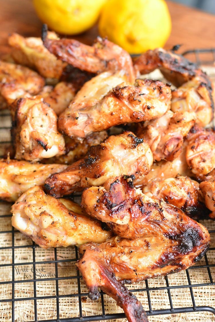 Grilled Chicken Wings stacked up on a cooling rack with lemons in the background 