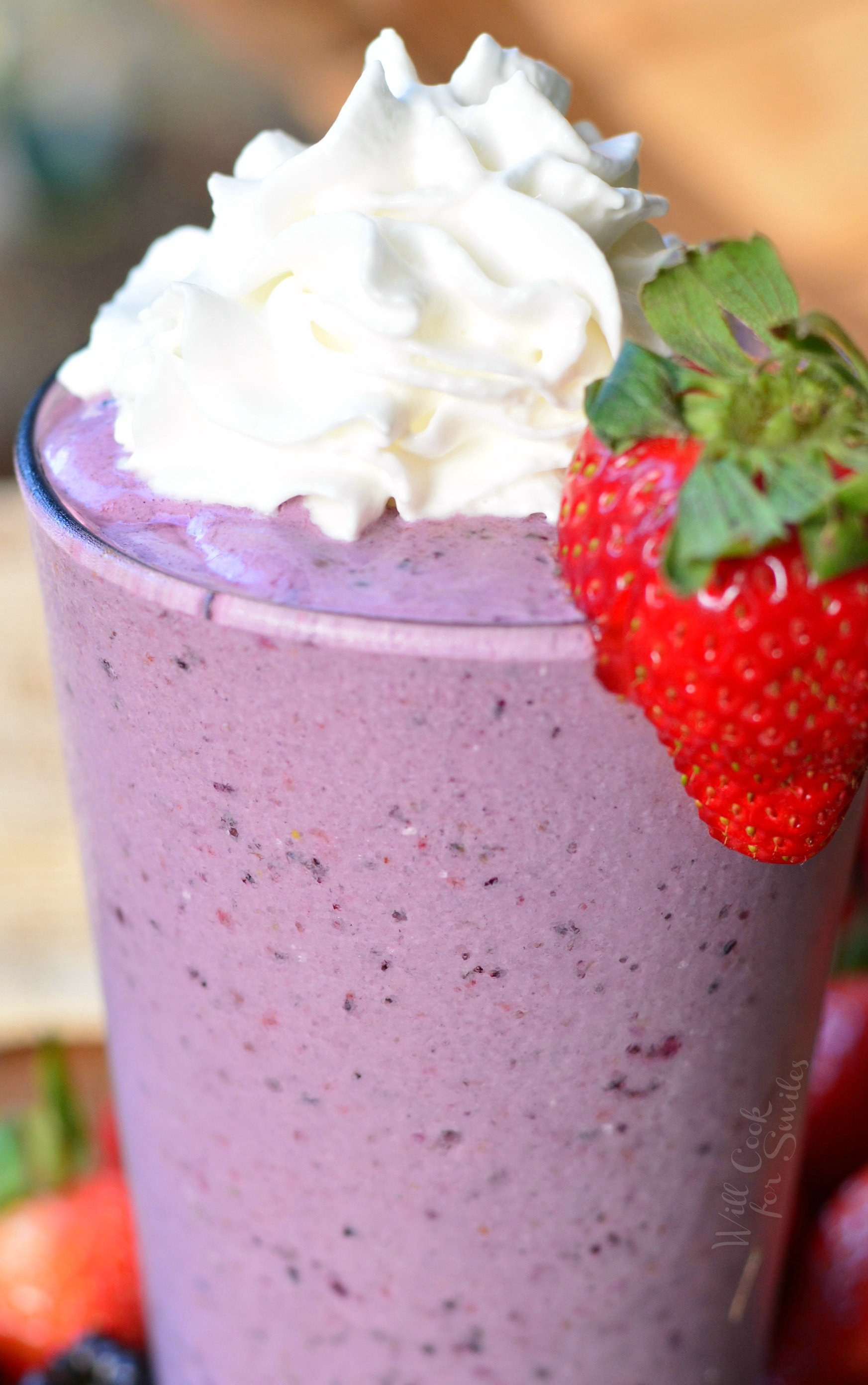 Berry Milkshake in a class with whip cream and strawberry to garnish on a wood table 