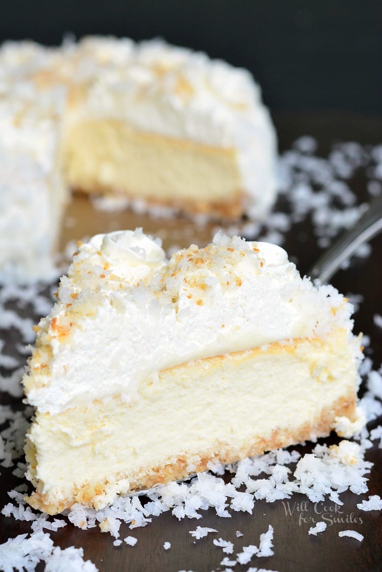 slice of coconut Cheesecake on a table with the rest of the cheesecake in the background 