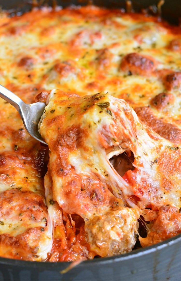 lifting some Cheesy Meatball Dip with a fork out of the pan 