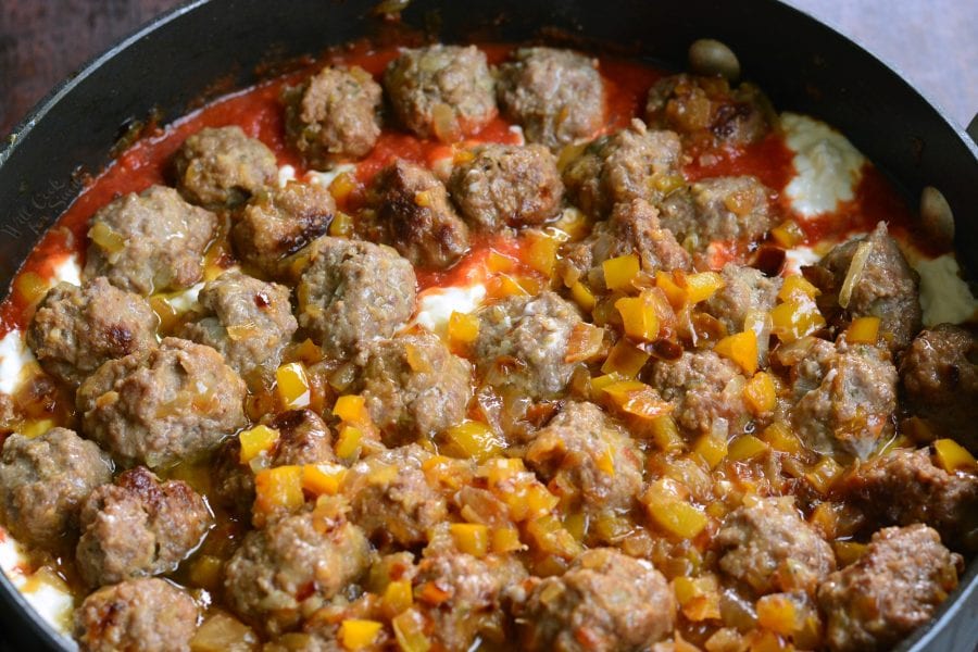 layered cheese, veggies, sauce, and meatballs in a cooking pan.
