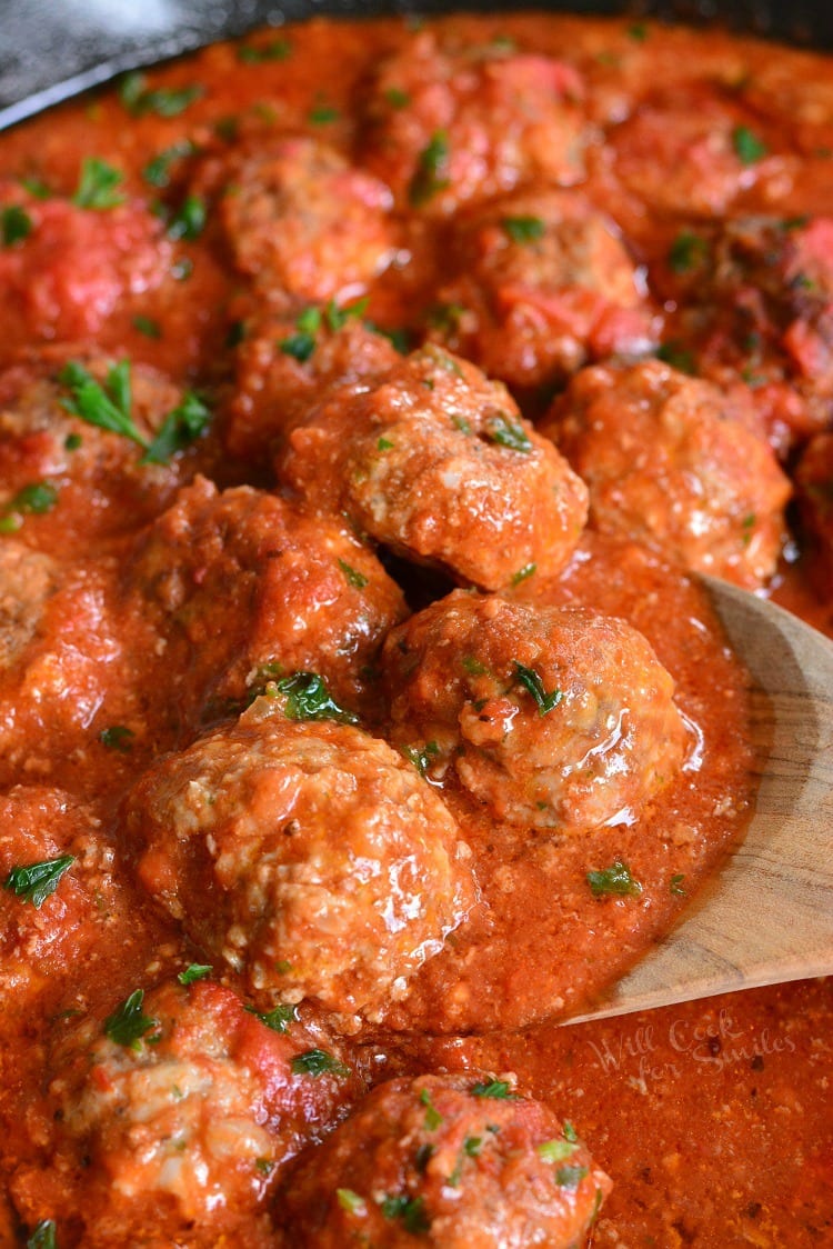 The BEST Italian Meatballs in a cast iron pan being scooped out by a wooden spoon 