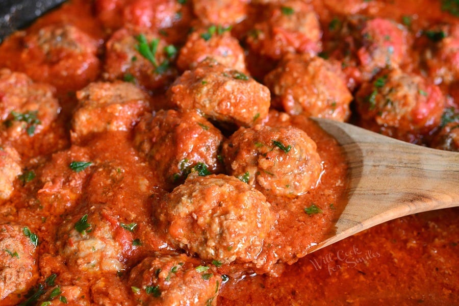 The BEST Italian Meatballs in a pan with a wooden spoon scoping them out 