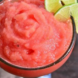 top of a frozen margarita in a glass with lime wedges as garnish.