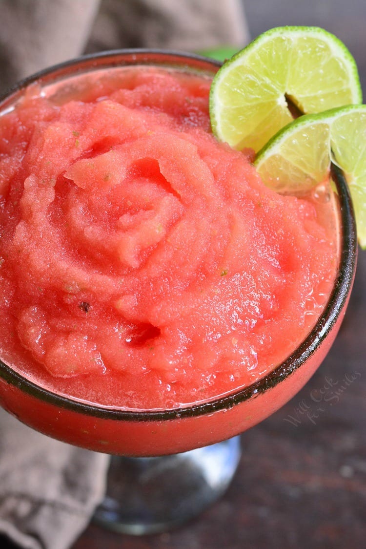 top of a frozen margarita in a glass with lime wedges as garnish.