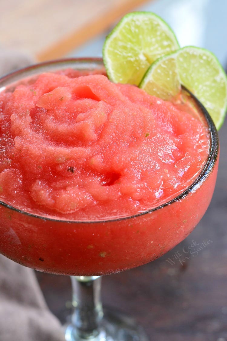 Watermelon frozen margarita in a margarita glass with limes on the rim of glass as garnish.
