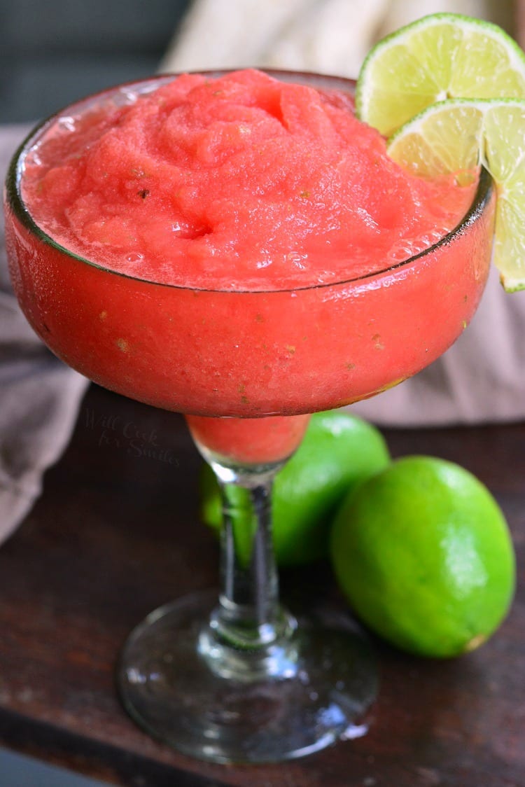 frozen watermelon margarita in a margarita glass with a lime on the rim.