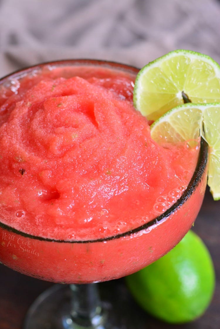 above shot of frozen margarita in a glass with limes on the side as garnish.