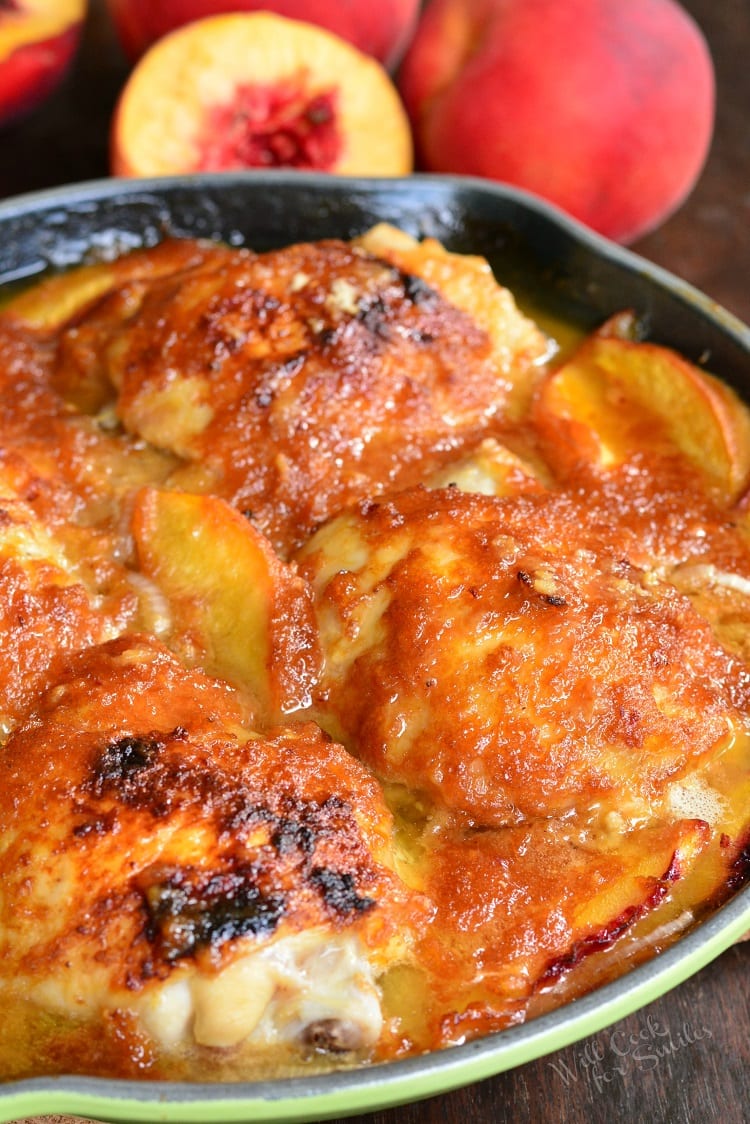 four chicken thighs with sauce and peaches in green cast iron pan and peaches on the background