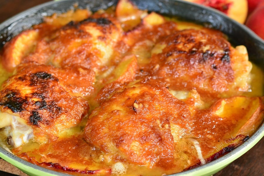 horizontal view of four chicken thighs with sauce and peaches in green cast iron pan 