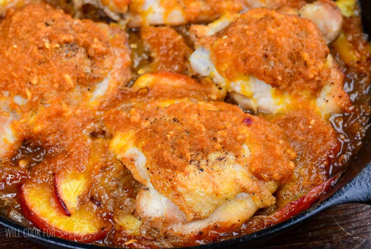 four juicy chicken thighs baked in peaches and peach sauce in a skillet.