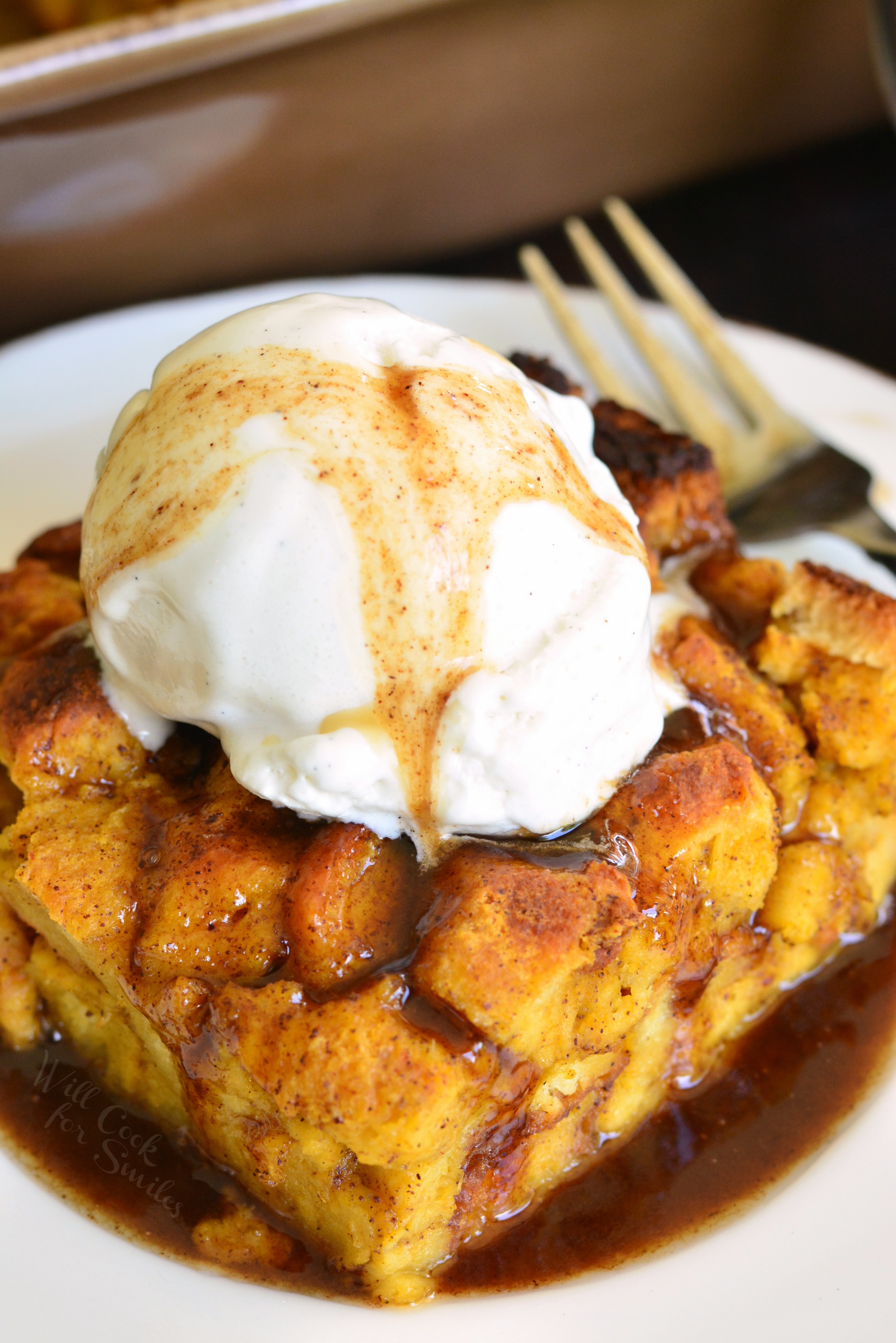 Brioche Pumpkin Bread Pudding on a plate topped with ice cream and syrup and fork