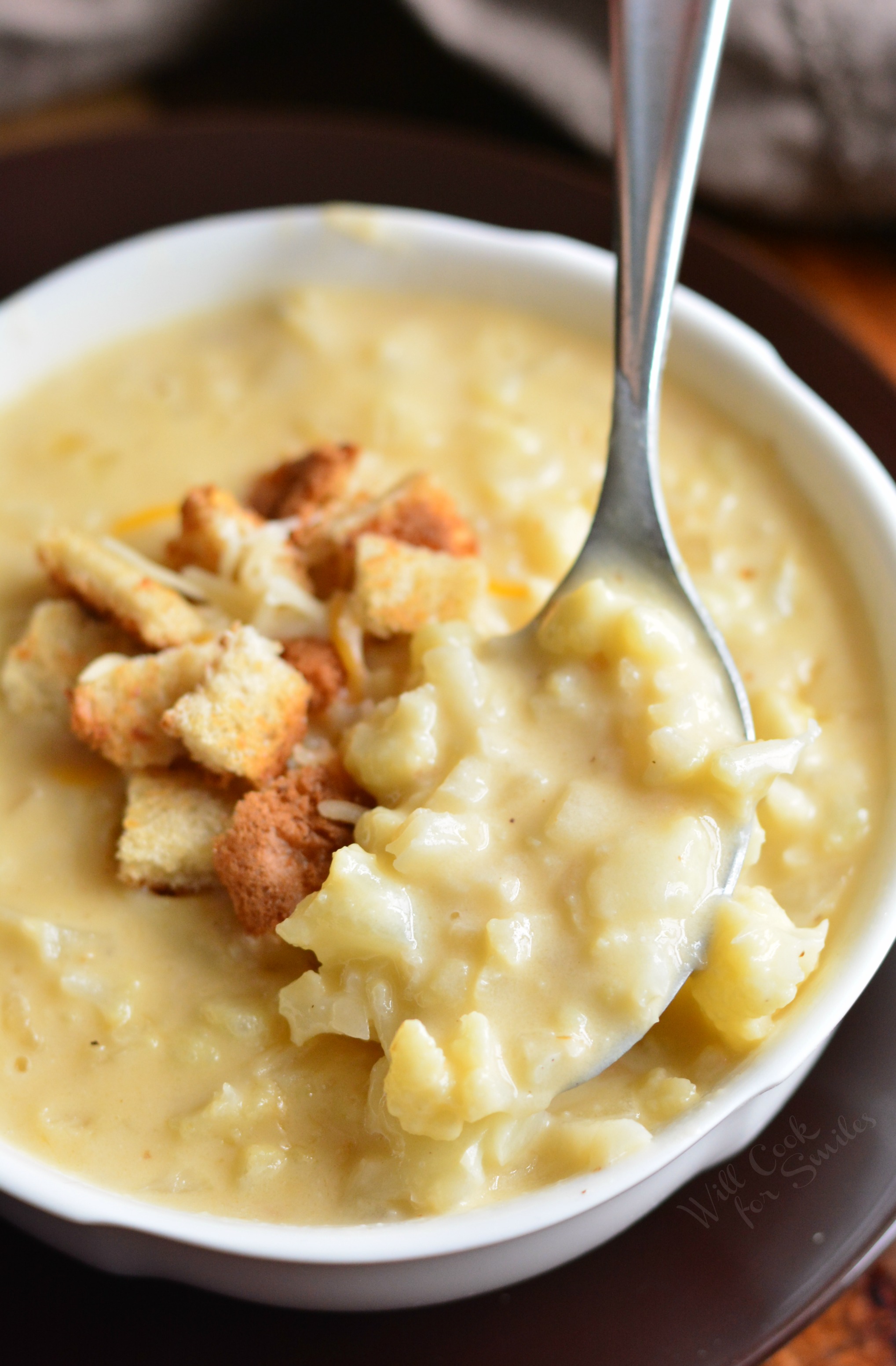 Cauliflower Cheese Soup in a bowl with croutons and cheese on tip with a spoon 