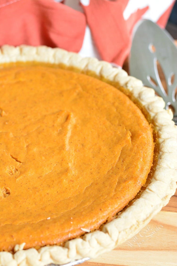 This PUMPKIN CHEESECAKE PIE on a table with a pie cutter in the background