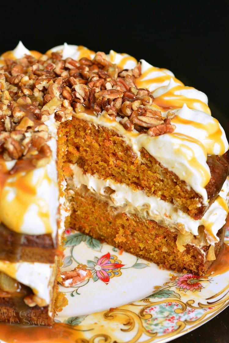 a whole apple carrot cake on a platter with one slice take out.