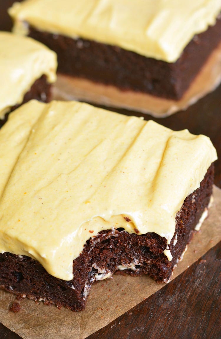 Frosted Pumpkin Brownies on parchment paper with bite taken out 