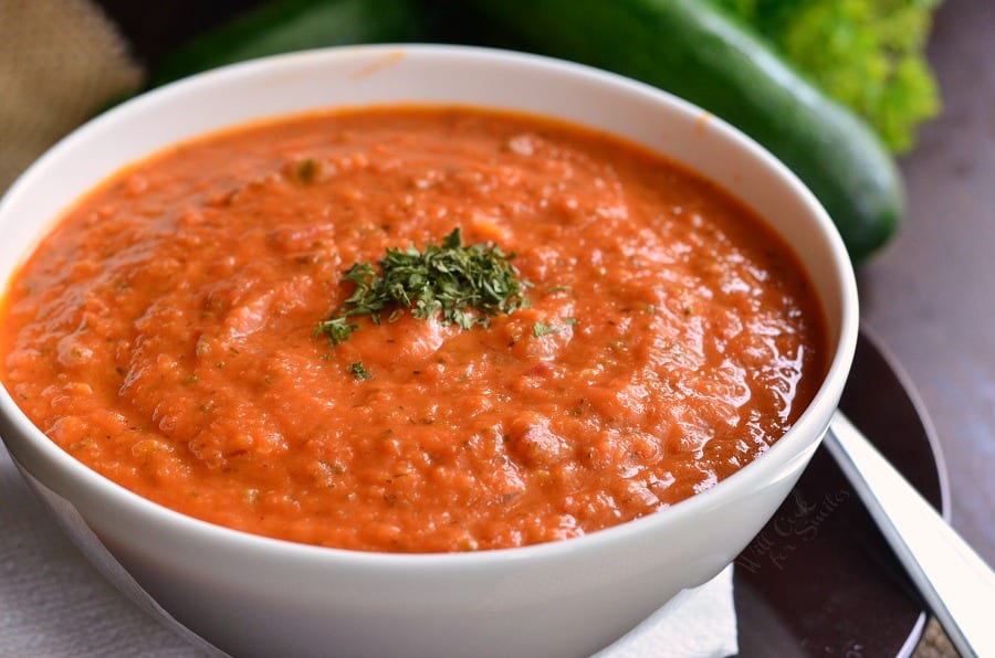 Zucchini Tomato Soup Recipe in a bowl that is on a plate with a spoon 