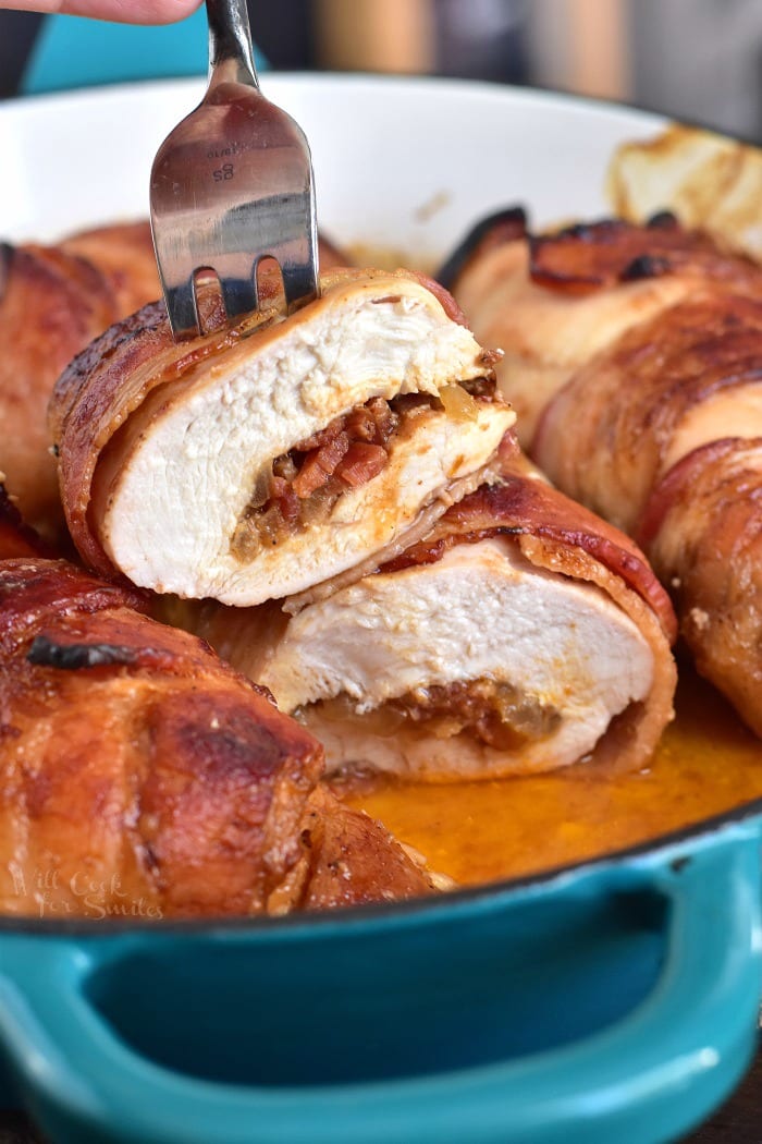 Bacon Wrapped BBQ Stuffed Chicken Breasts in a pan with one sliced in half and a fork through it 