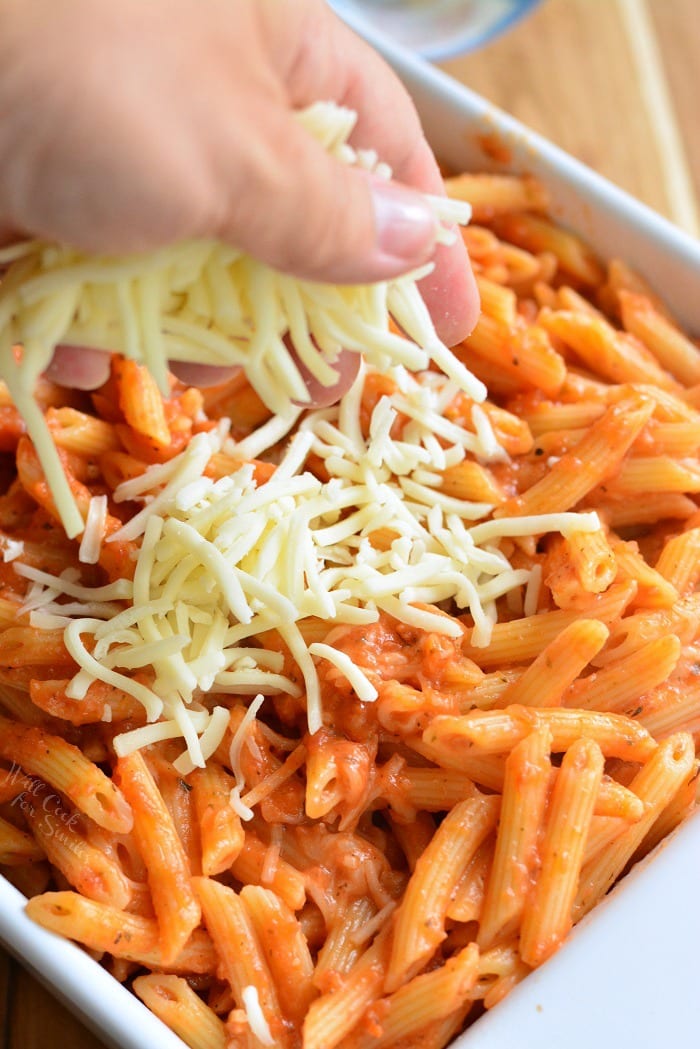 pouring cheese over the pasta that is in a baking dish 