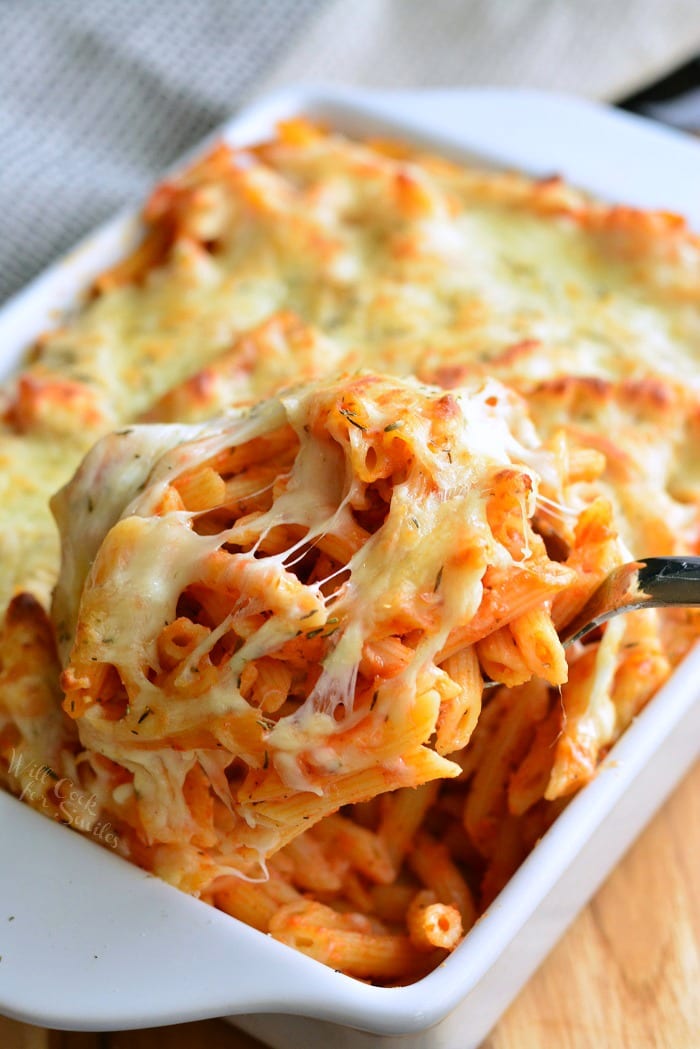 Homemade Basil Roasted Garlic Baked Penne in a baking dish with some being scooped out with metal spoon 