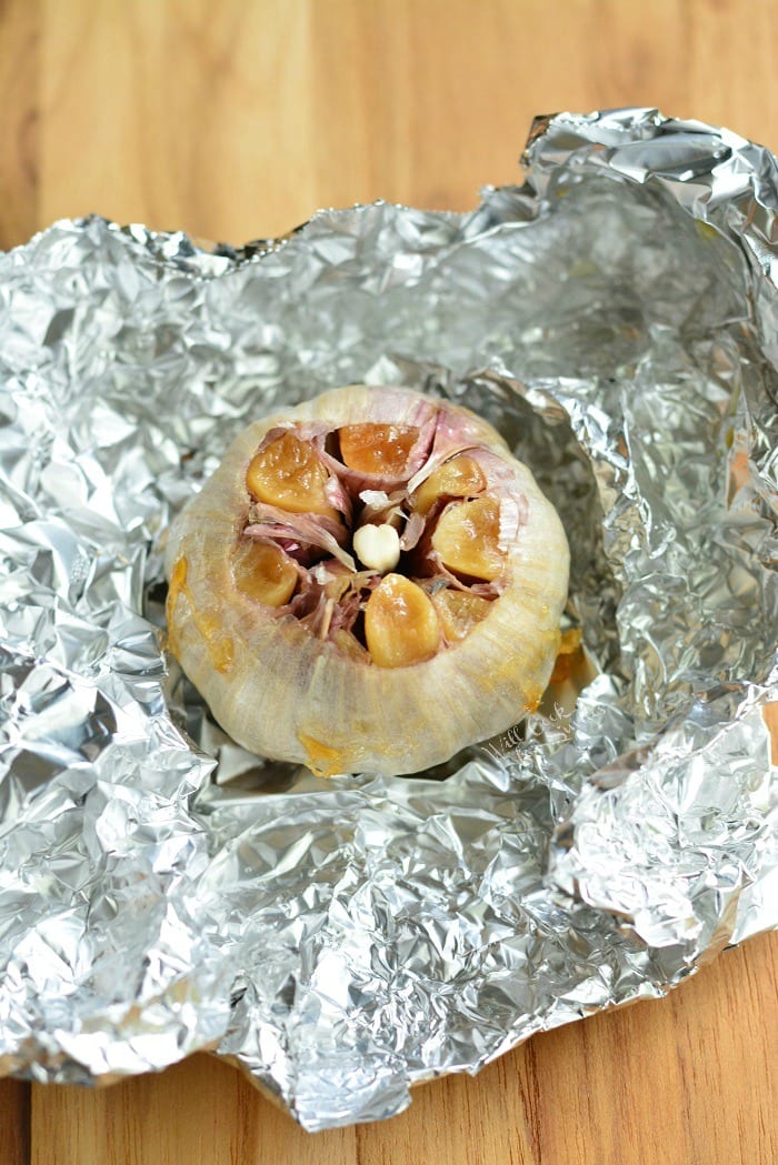 roasted garlic laying on tin foil on a wood cutting board 