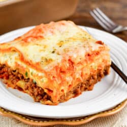A slice of lasagna with a fork on a stack of two plates.