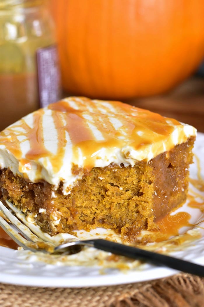 a slice of pumpkin poke cake soaked with salted caramel and topped with smooth cream cheese frosting with bite taken out.