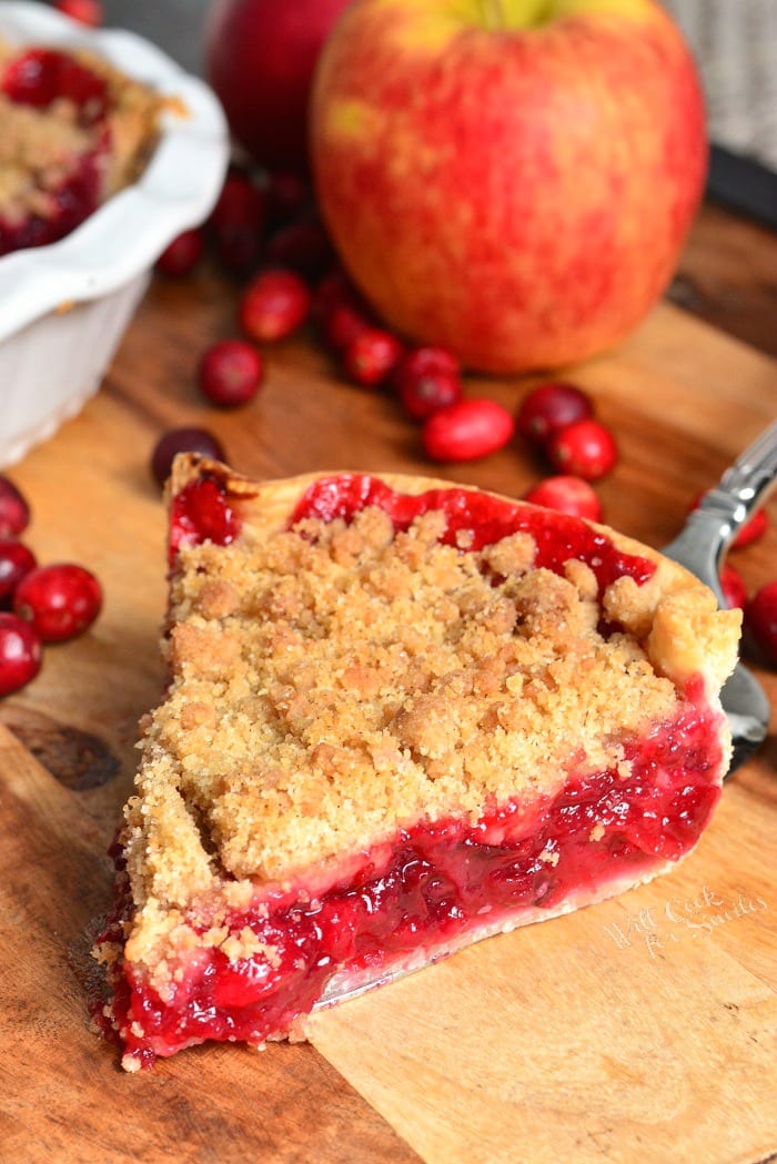 slice of Apple Cranberry Pie on a cutting board with apples and cranberries 