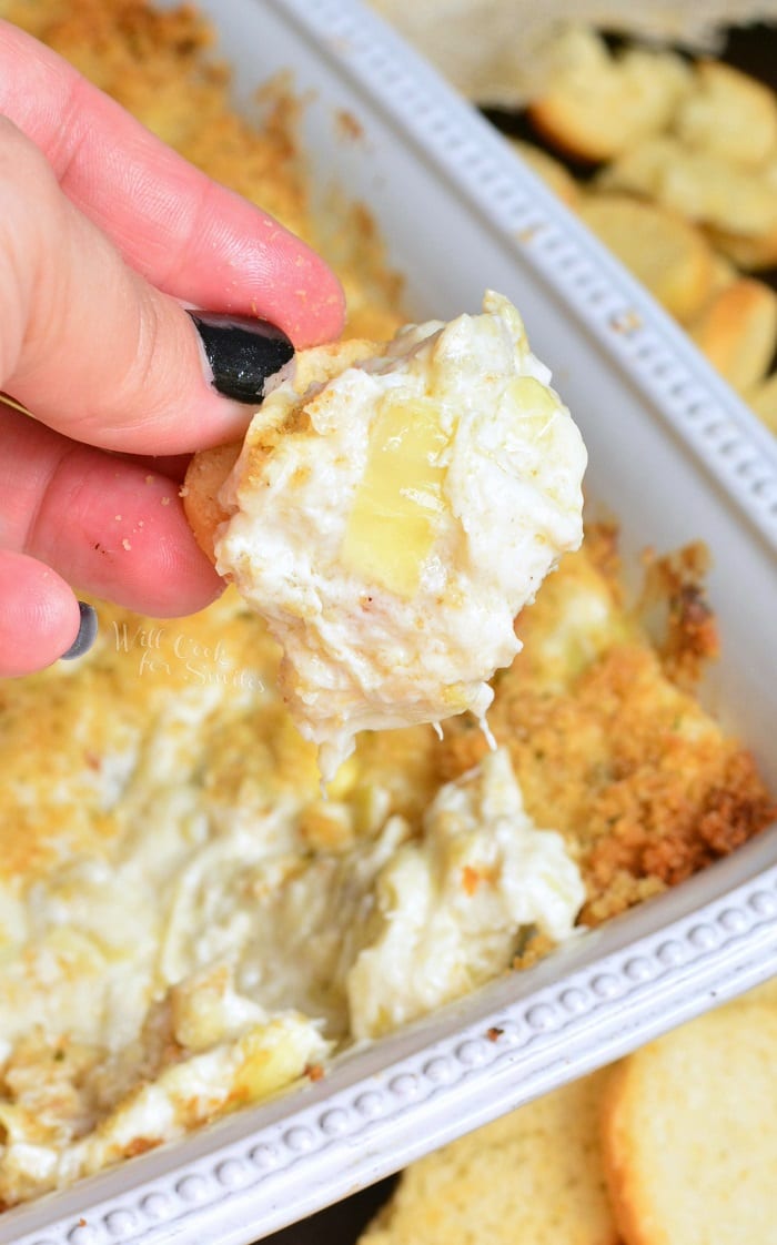 dipping bagel dip in Creamy Crab and Artichoke Dip that in a baking dish 