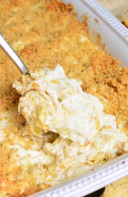 spooning creamy artichoke dip with a spoon from the baking dish