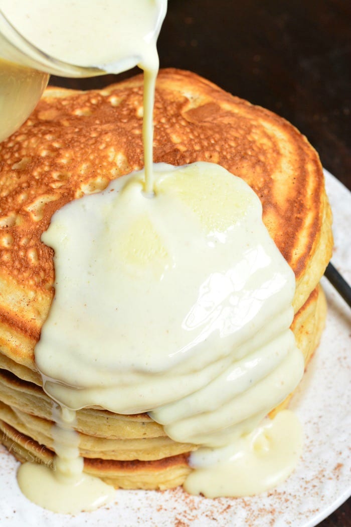 pouring Eggnog sauce over Pancakes that are on a plate 