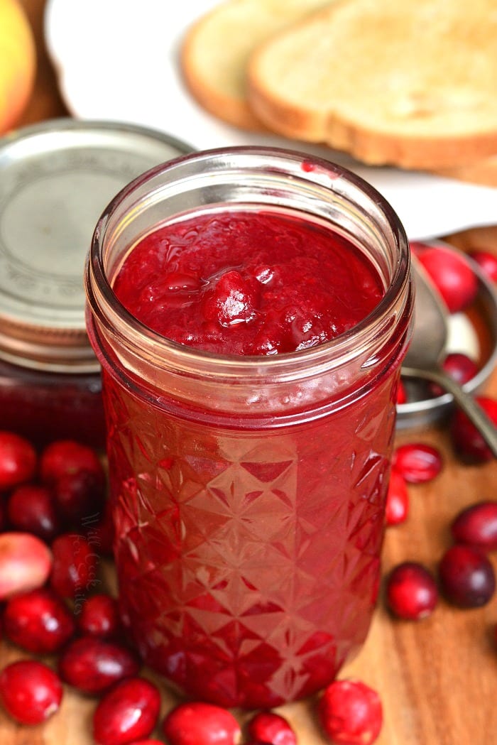 Cranberry Jam in a jar with out the lid on a cutting board and fresh cranberries around it 