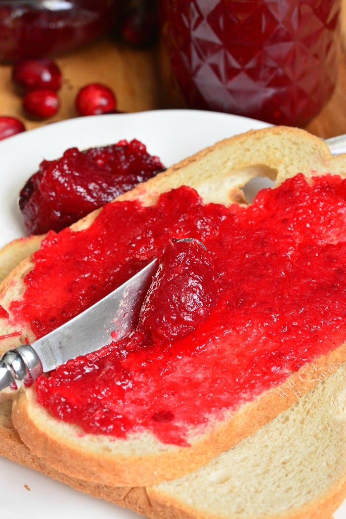 spreading Cranberry Jam on toast with a butter knife that is on white plate 