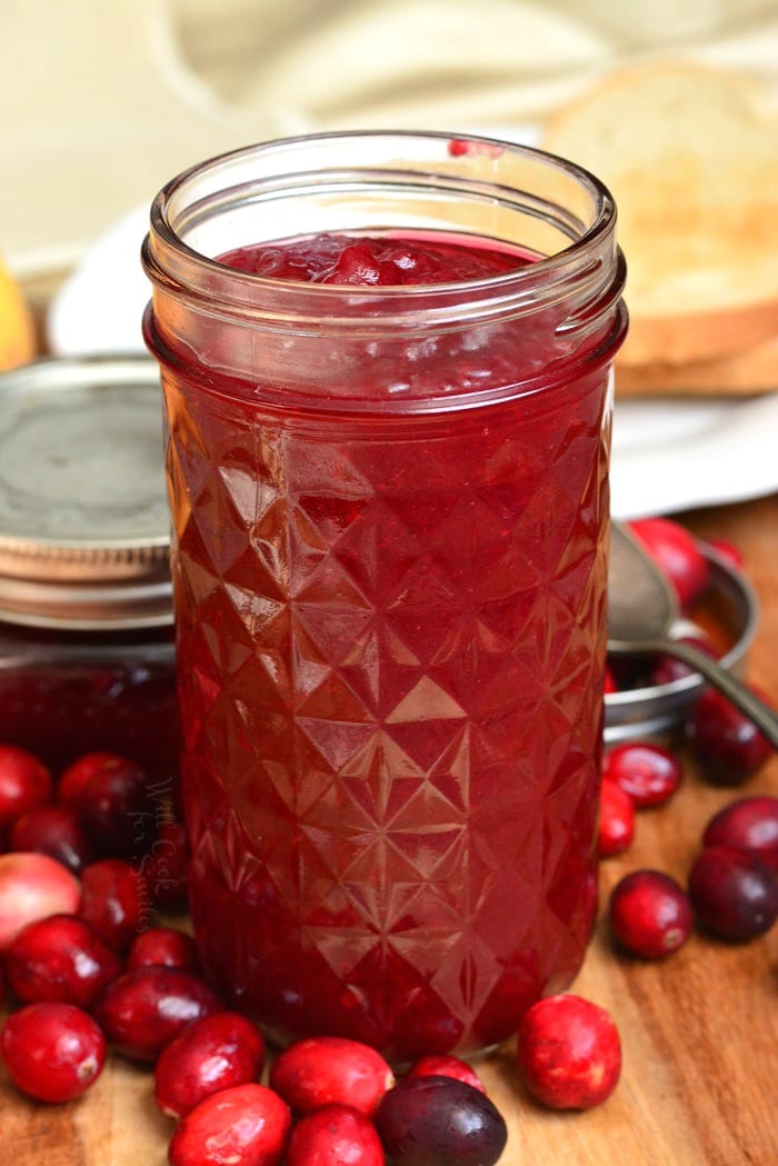 Cranberry Jam in a mason jar on a wood cutting board and fresh cranberries around it 