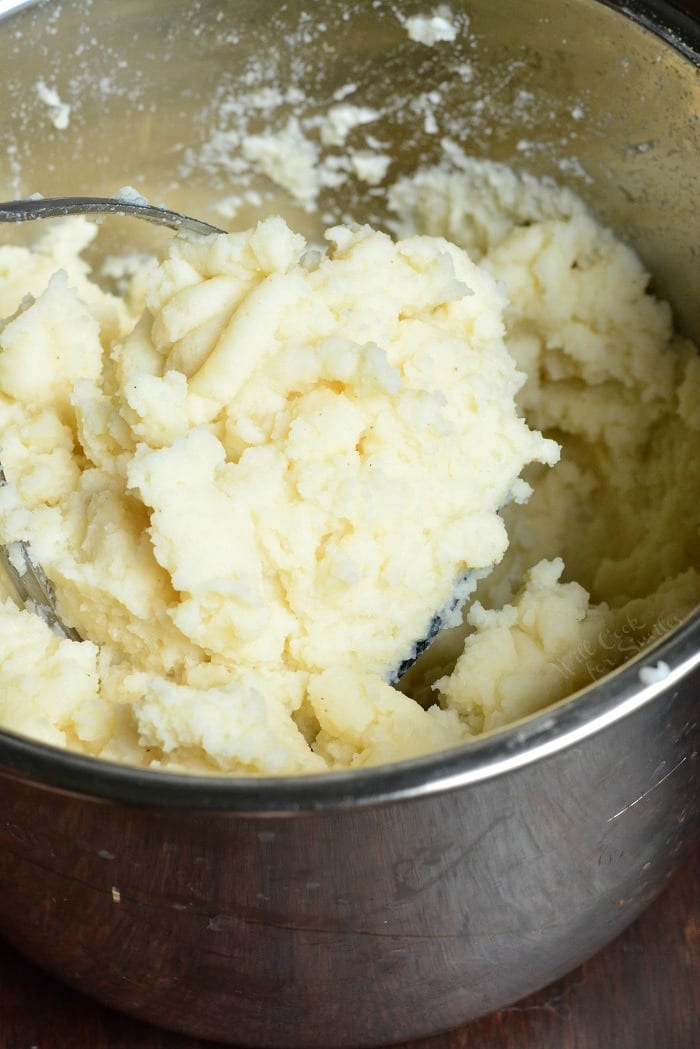 Garlic Mashed Potatoes in a bowl with a potato masher 