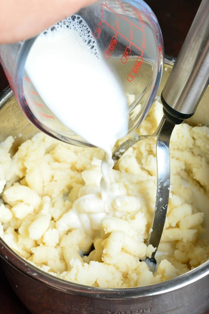 pouring milk in bowl with Garlic Mashed Potatoes with a potato masher 