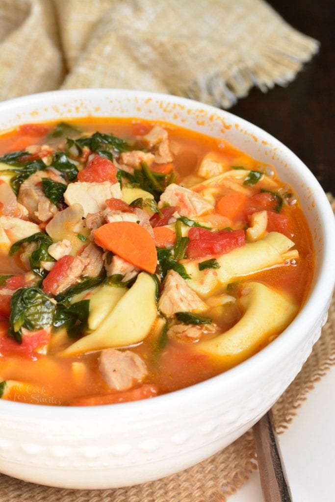 side view of white bowl with turkey tortellini soup.