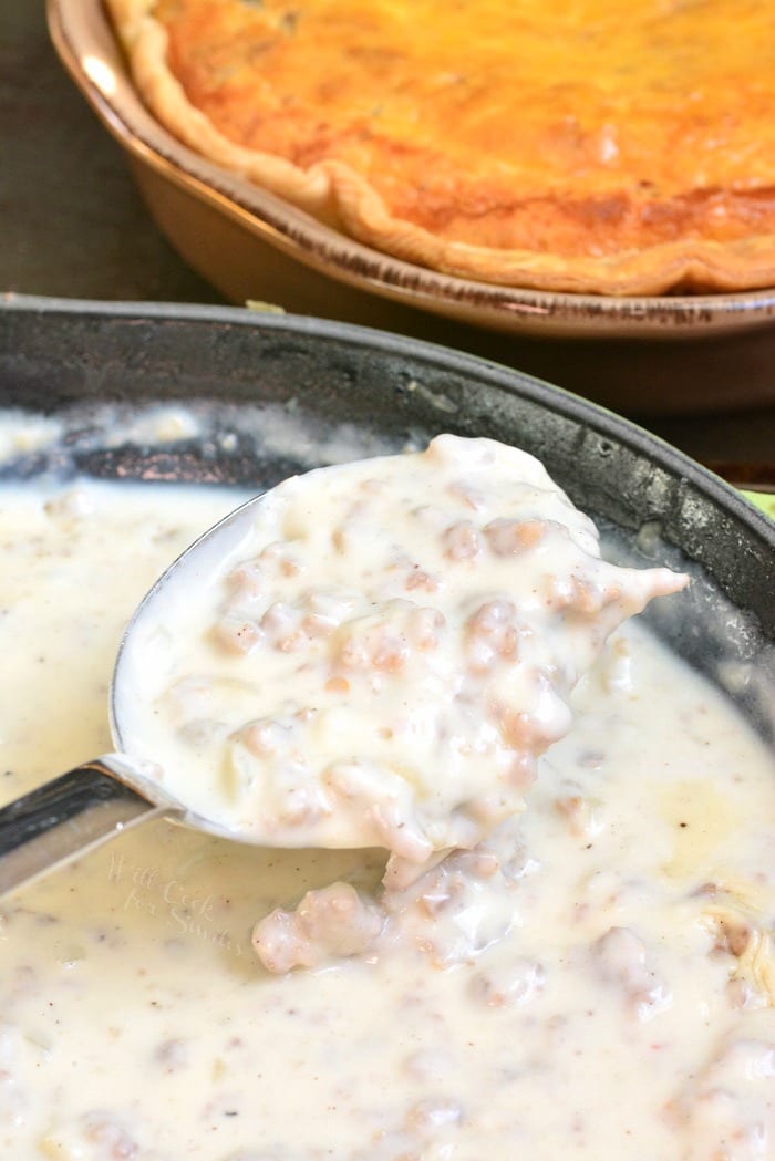 Sausage gravy in a pan with a spoon stirring.