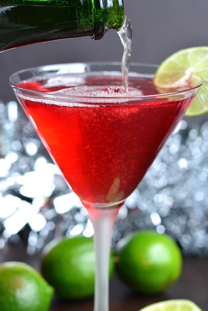 Cosmopolitan champagne cocktail in a martini glass on a cutting board with limes