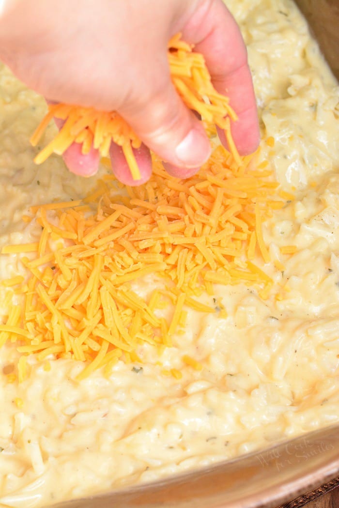 spreading shredded cheddar cheese on tom of mixed hashbrown mixture in a casserole pan