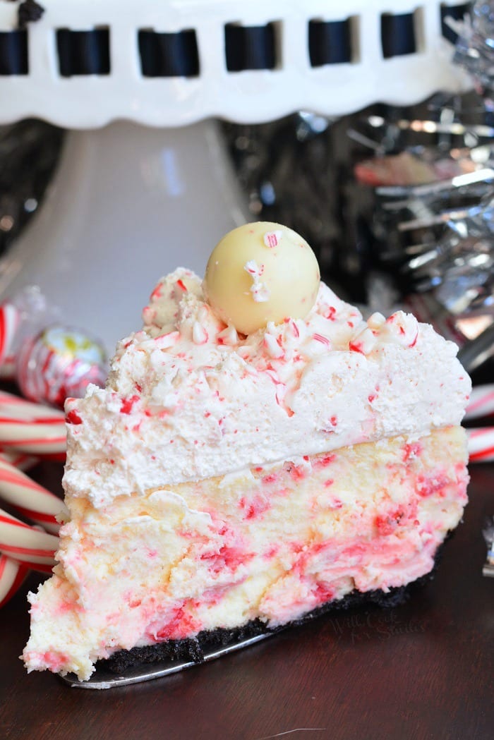 piece of Peppermint Cheesecake on a wood table with candy cans and cake stand in the background 