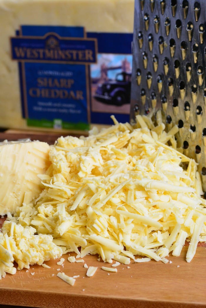 Shredded Westminster Sharp Cheddar Cheese on a cutting board with a cheese shredder 