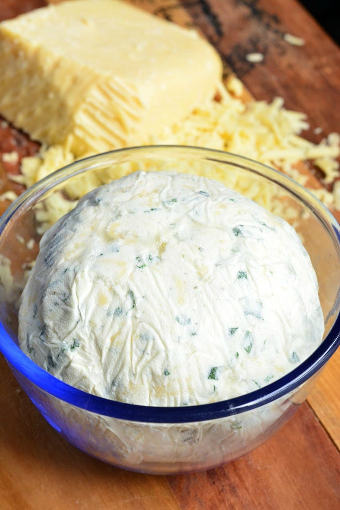 Cheddar Cheese Ball in a glass bowl with shredded cheese on a cutting board 